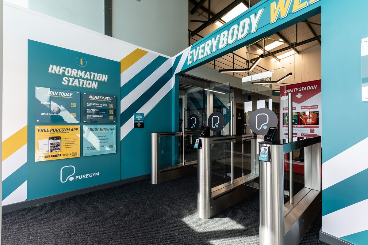 PureGym Coleraine: Security station with turnstiles, information displays promoting free phone service.