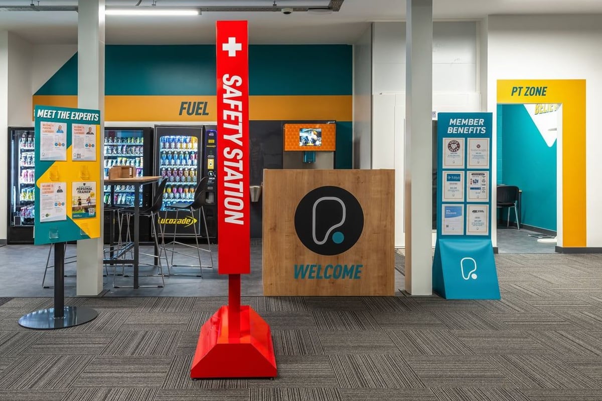 PureGym Llantrisant: Vending machines, seating area, and welcome signage in a commercial building lobby.