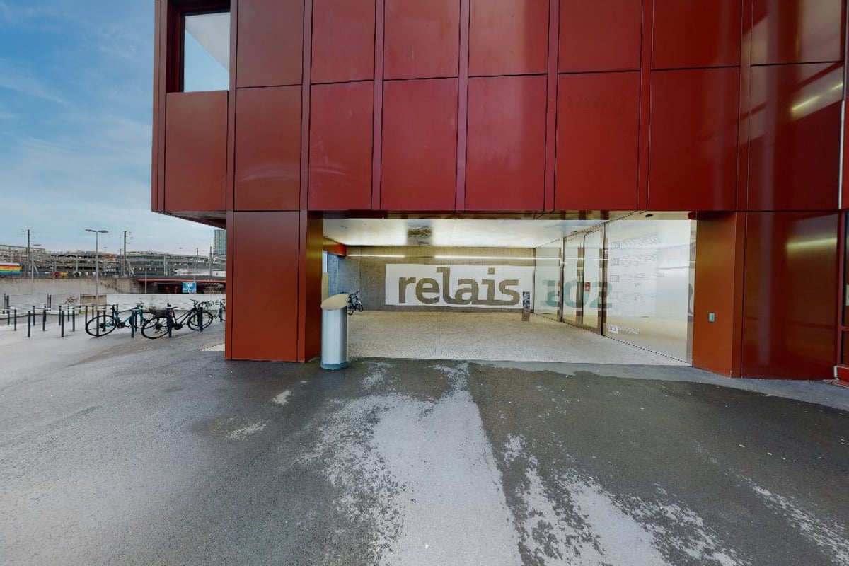 PureGym Aarau: Signalisation du relais visible sous une structure rouge vif avec vélos garés à l'extérieur, sol enneigé.