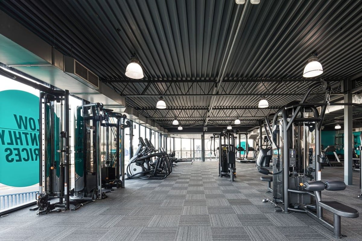 PureGym Dudley Tipton: Gym floor with squat racks, weight machines, rubberized flooring, and industrial ceiling lamps.