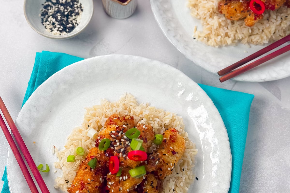Two plates of crispy chicken with rice, garnished with spring onions and red chili slices
