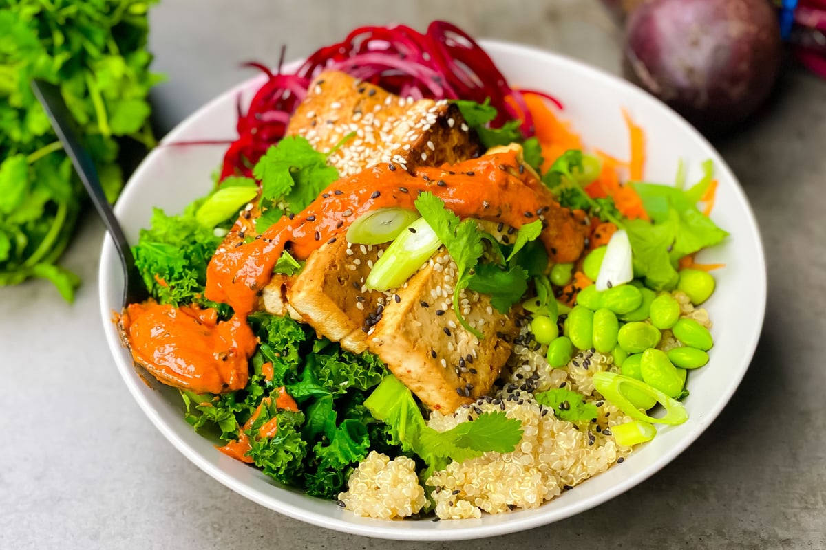 Bowl of quinoa topped with glazed tofu, edamame, kale, beetroot and spring onion