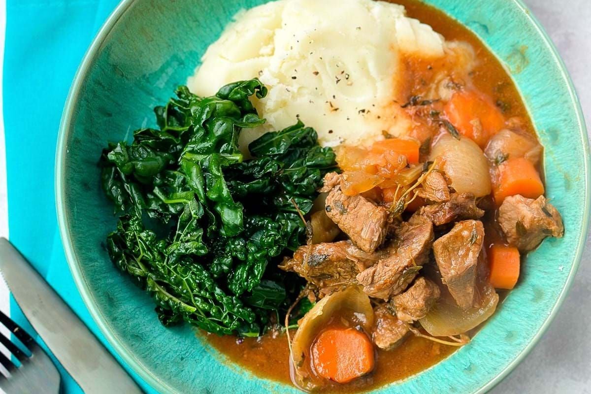 Mashed potatoes, cooked kale, and beef stew with carrots and onions in a bowl