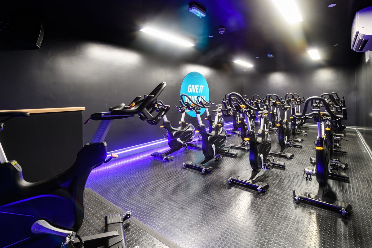 PureGym London Lambeth: Rows of stationary bikes, free weights and mirrored walls in a dimly lit studio space.