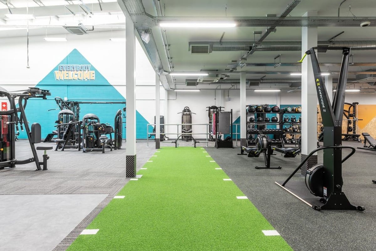 PureGym Ormskirk: Weightlifting platforms, resistance machines, green turf area, and free weight racks in a spacious gym.
