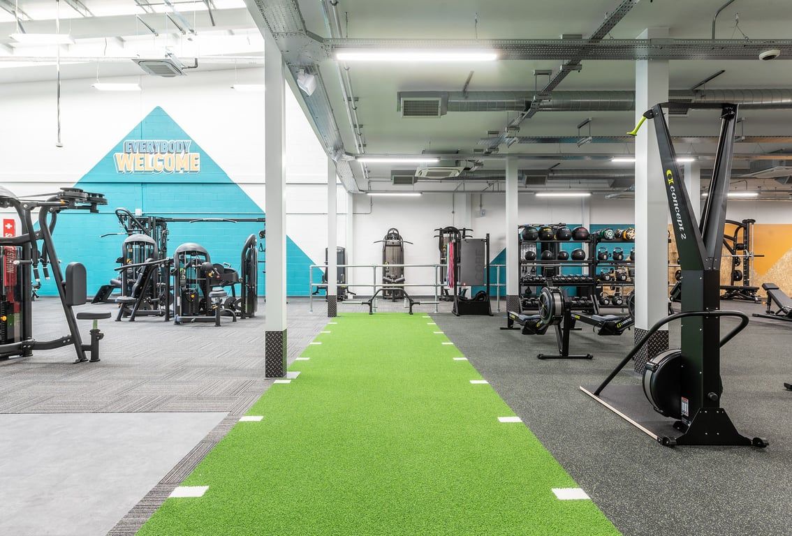 PureGym Ormskirk: Weightlifting platforms, resistance machines, green turf area, and free weight racks in a spacious gym.