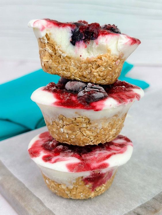 Stack of three frozen yoghurt and berry oat cups on a white surface with a blue cloth in b