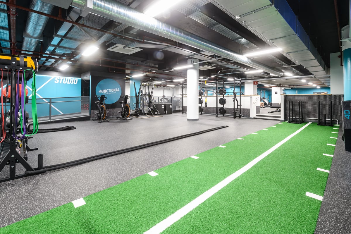 PureGym London East India Dock: Functional training area, green turf, resistance machines, free weights, and studio signage.