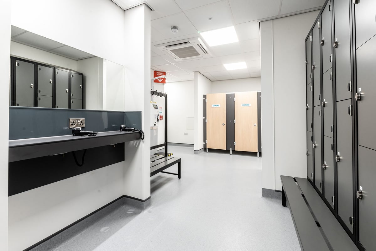 PureGym Nottingham West Bridgford: Rows of grey lockers, benches, and white walls - a utilitarian changing room.