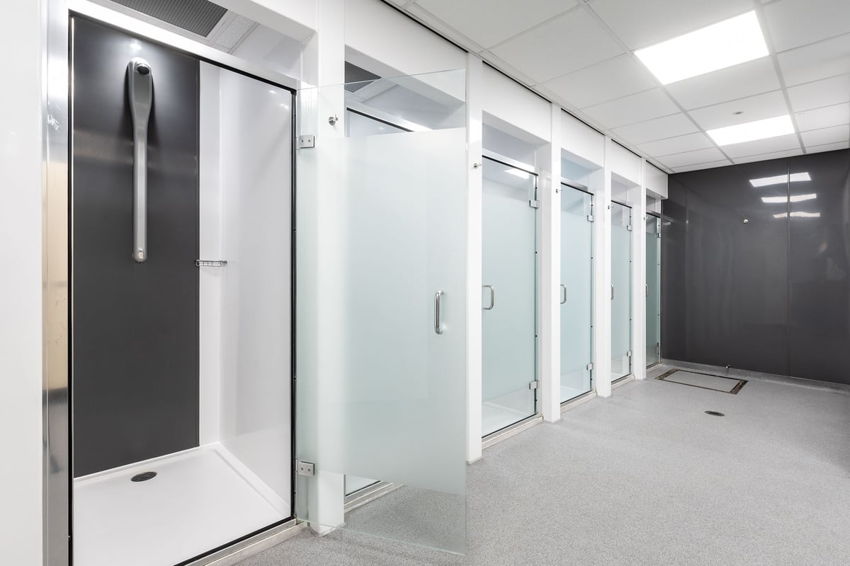 PureGym London Limehouse: Row of shower stalls with frosted glass doors and tiled floors.