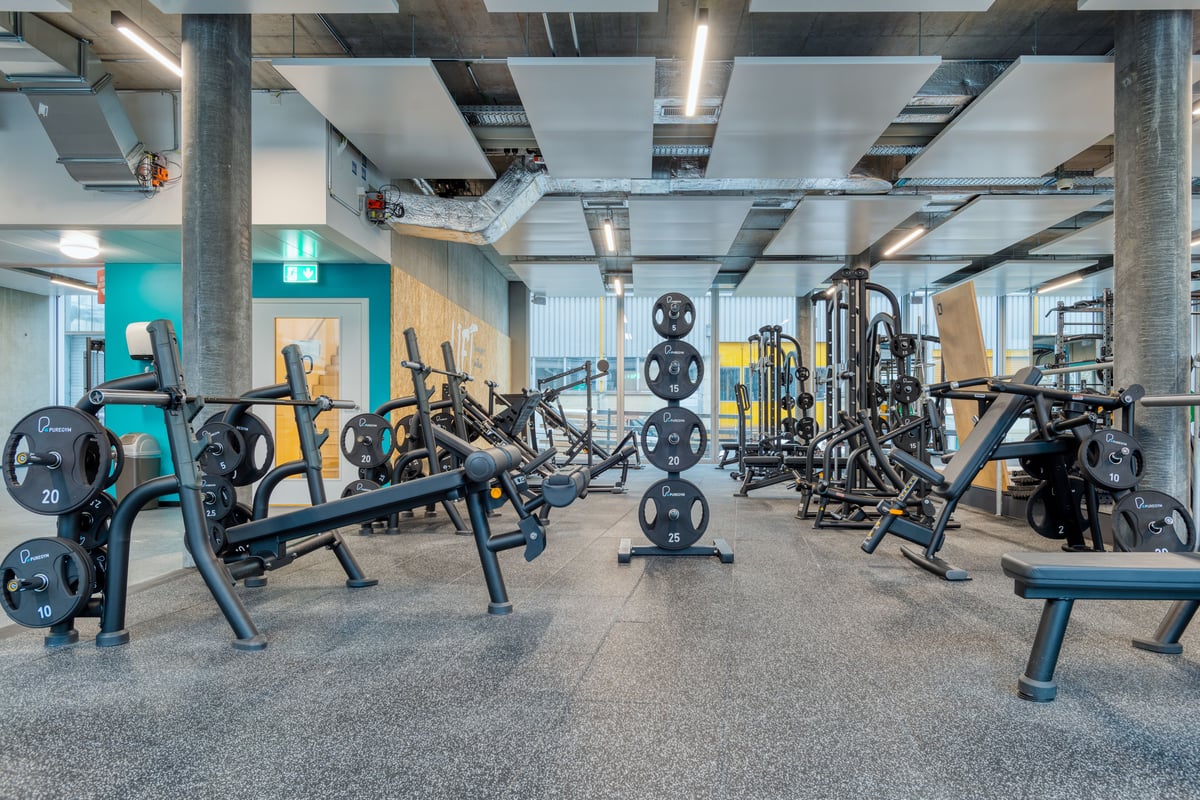 PureGym Zürich Oerlikon: Weitwinkelansicht des Freihantelbereichs mit Bänken, Kurzhanteln und Squat Racks.