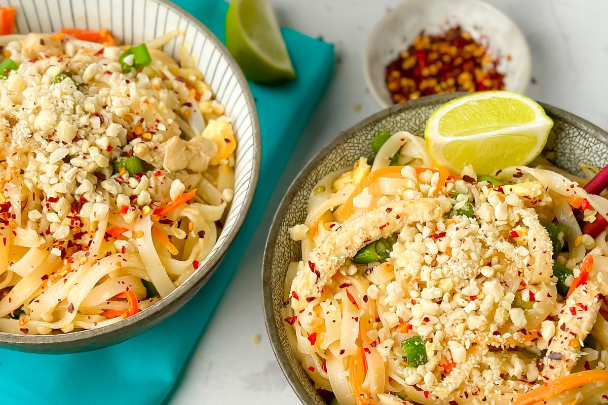 Two bowls of rice noodles topped with crushed peanuts, vegetables and lime wedge