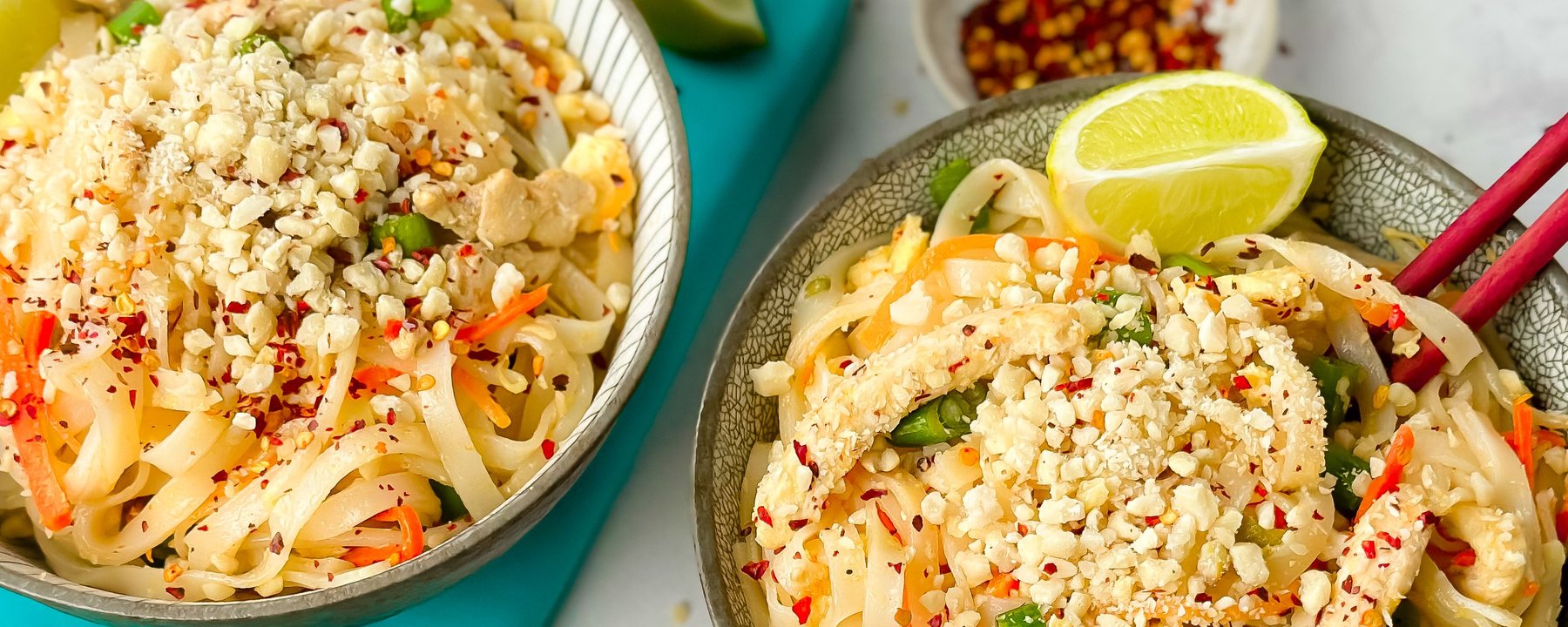 Two bowls of rice noodles topped with crushed peanuts, vegetables and lime wedge