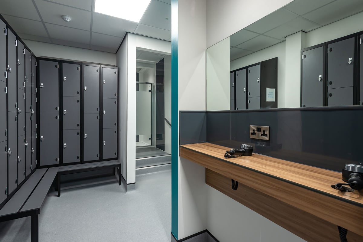 PureGym Stratford-upon-avon: Rows of lockers, wooden benches, and vanity mirrors in a changing room setting.