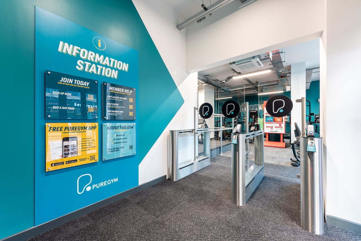 PureGym London Palmers Green: Information station, turnstiles, advertisement for a free Pure Gym app.