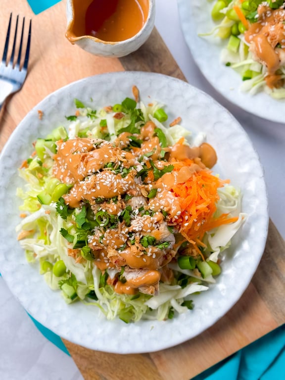 Salad with shredded cabbage, carrots, green onions, chicken, sesame seeds, and peanut sauce