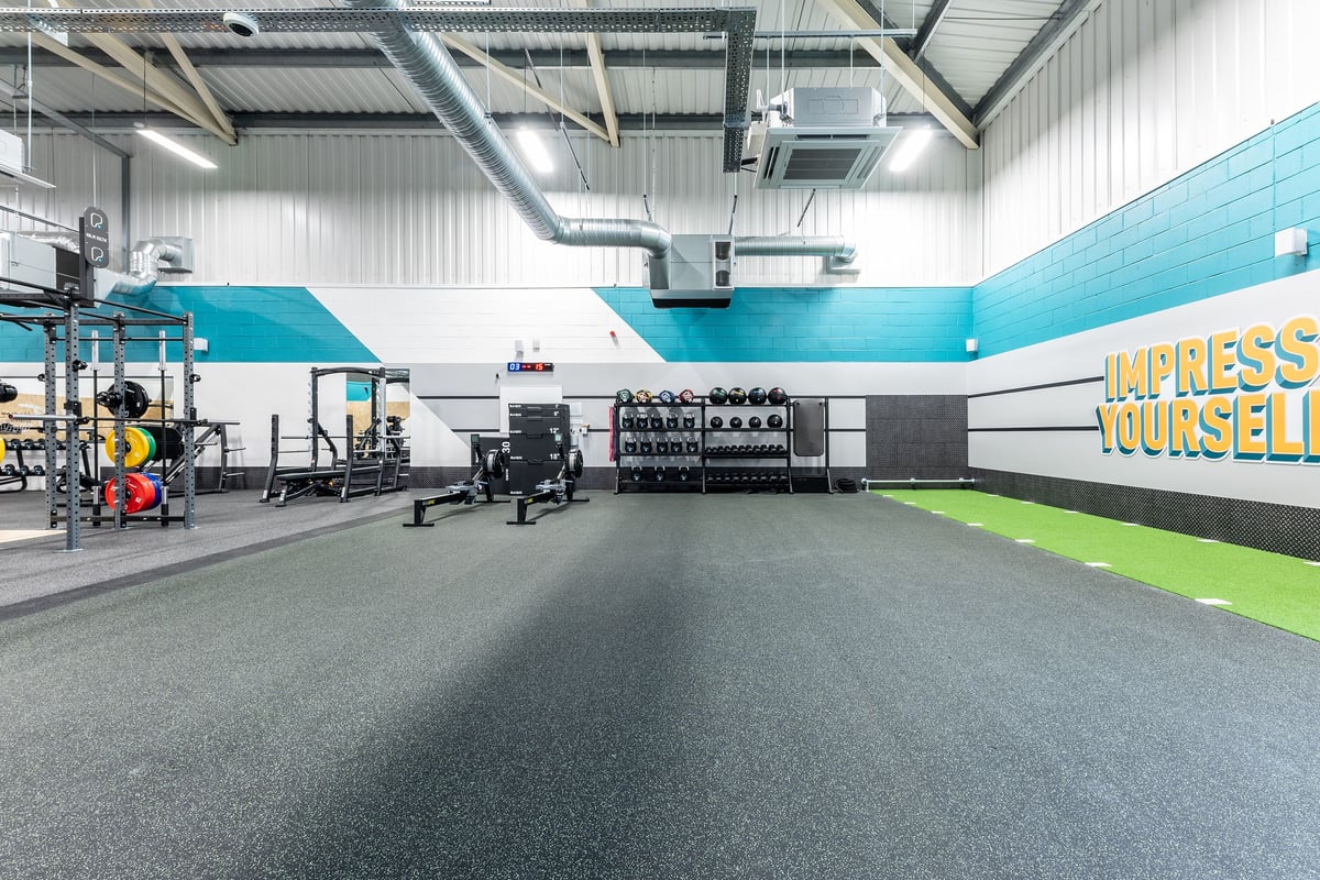 PureGym Merthyr Tydfil: Functional training area with weight racks, exercise balls, rubberized flooring, and wall graphics.