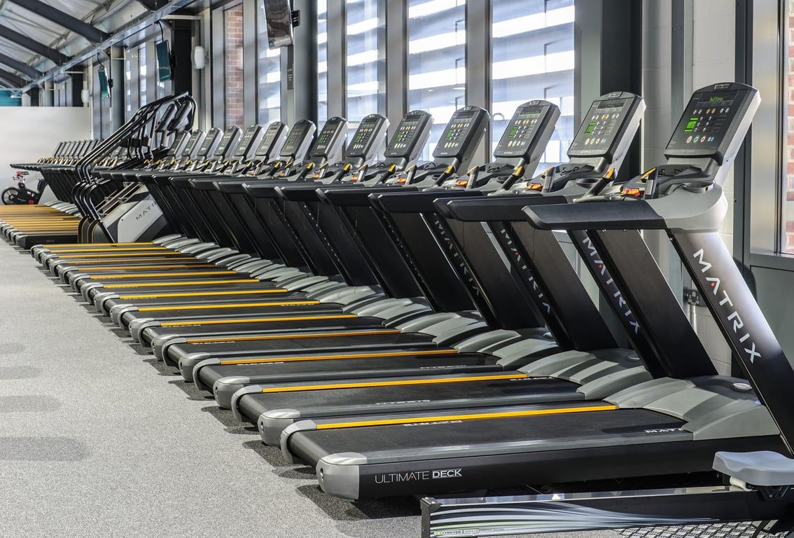 PureGym Leeds Kirkstall Bridge: Rows of treadmills with digital displays lining a bright indoor facility.