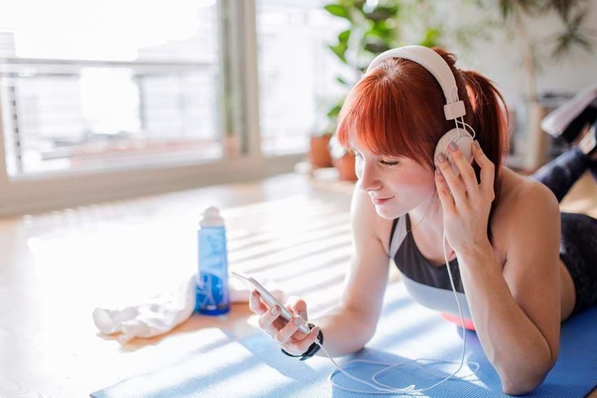 Young woman with red hair lying on a mat listening to music with headphones indoors