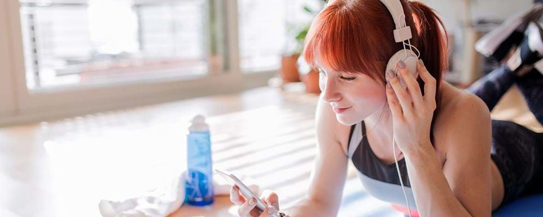 Young woman with red hair lying on a mat listening to music with headphones indoors