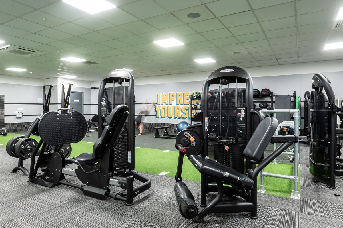 PureGym Epsom: Rows of resistance machines, weighted cable pulleys, and green turf flooring in a fitness studio.