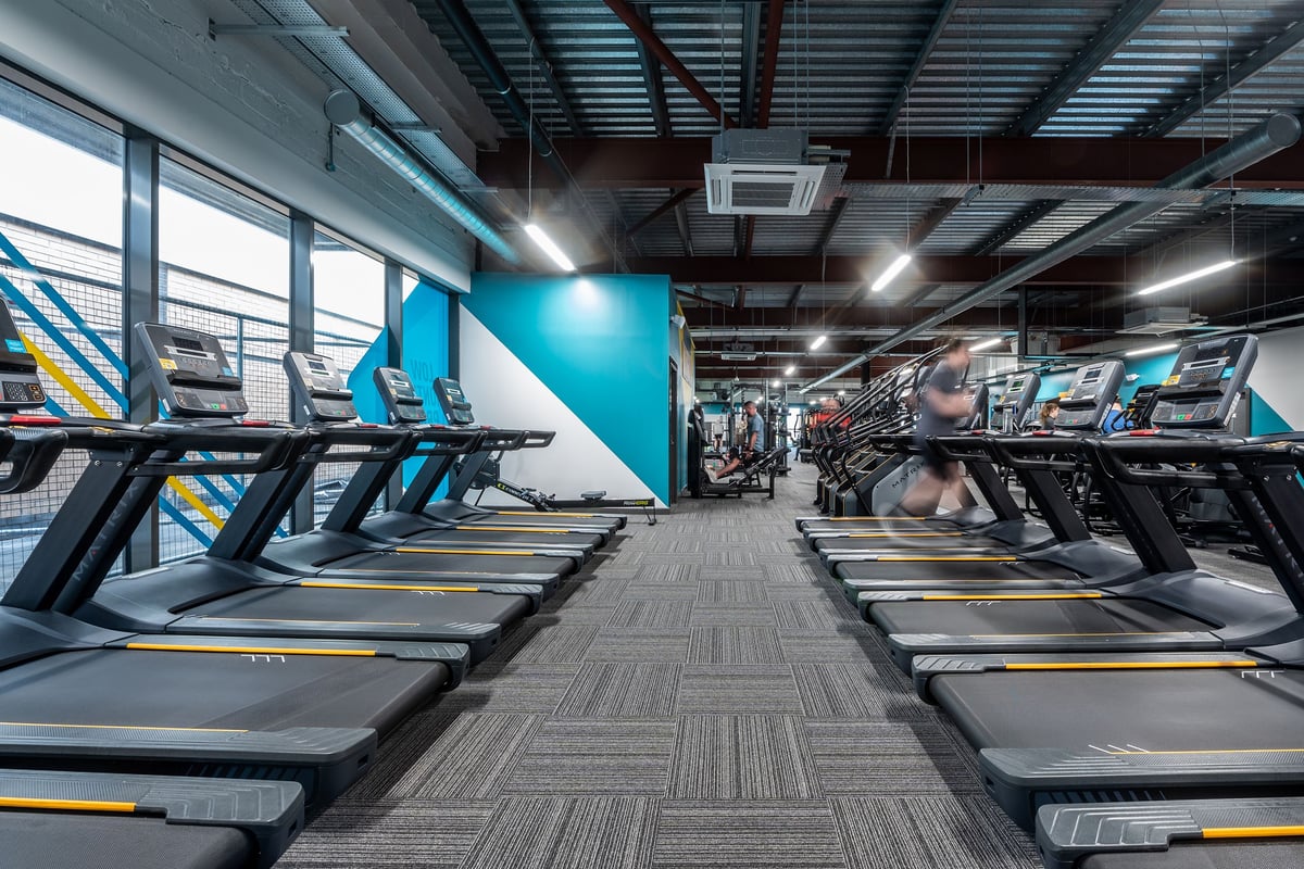 PureGym Craigavon: Rows of treadmills, rubberized flooring, exposed ceiling ducts in a modern gym interior.