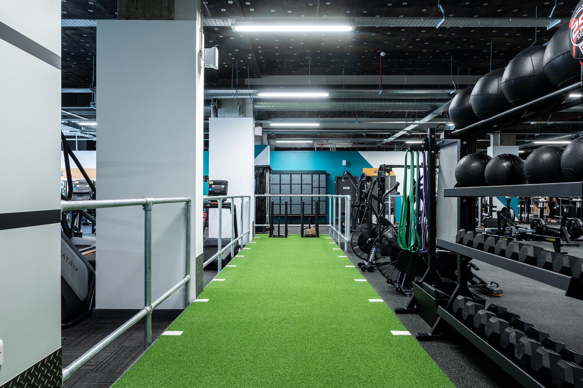 PureGym London Beckenham: Green turf area with weight racks, dumbbells, and benches in a gym setting.