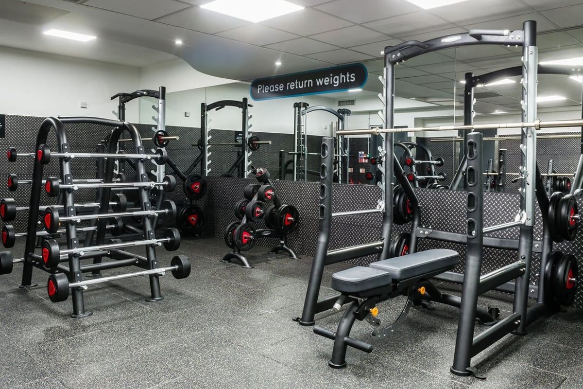 PureGym London Holborn: Gym with squat racks, weight benches, rubberized floors, mirrors, and weight racks with red plates.