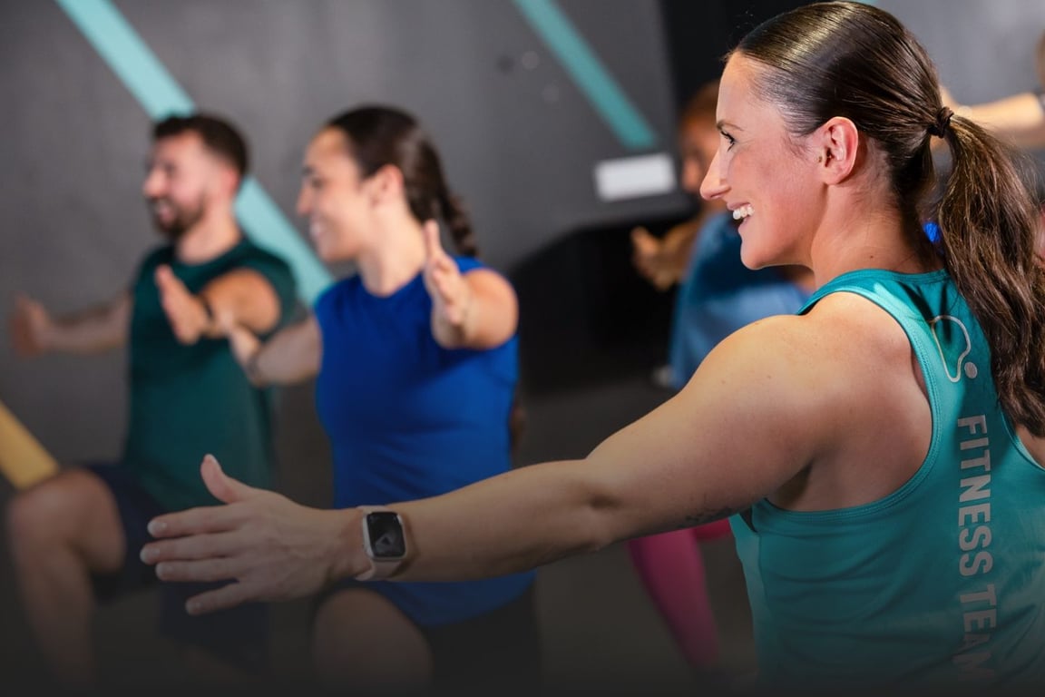 HIIT Training led by a female PureGym coach with a male and a female member in a blurry background lifting their knees.