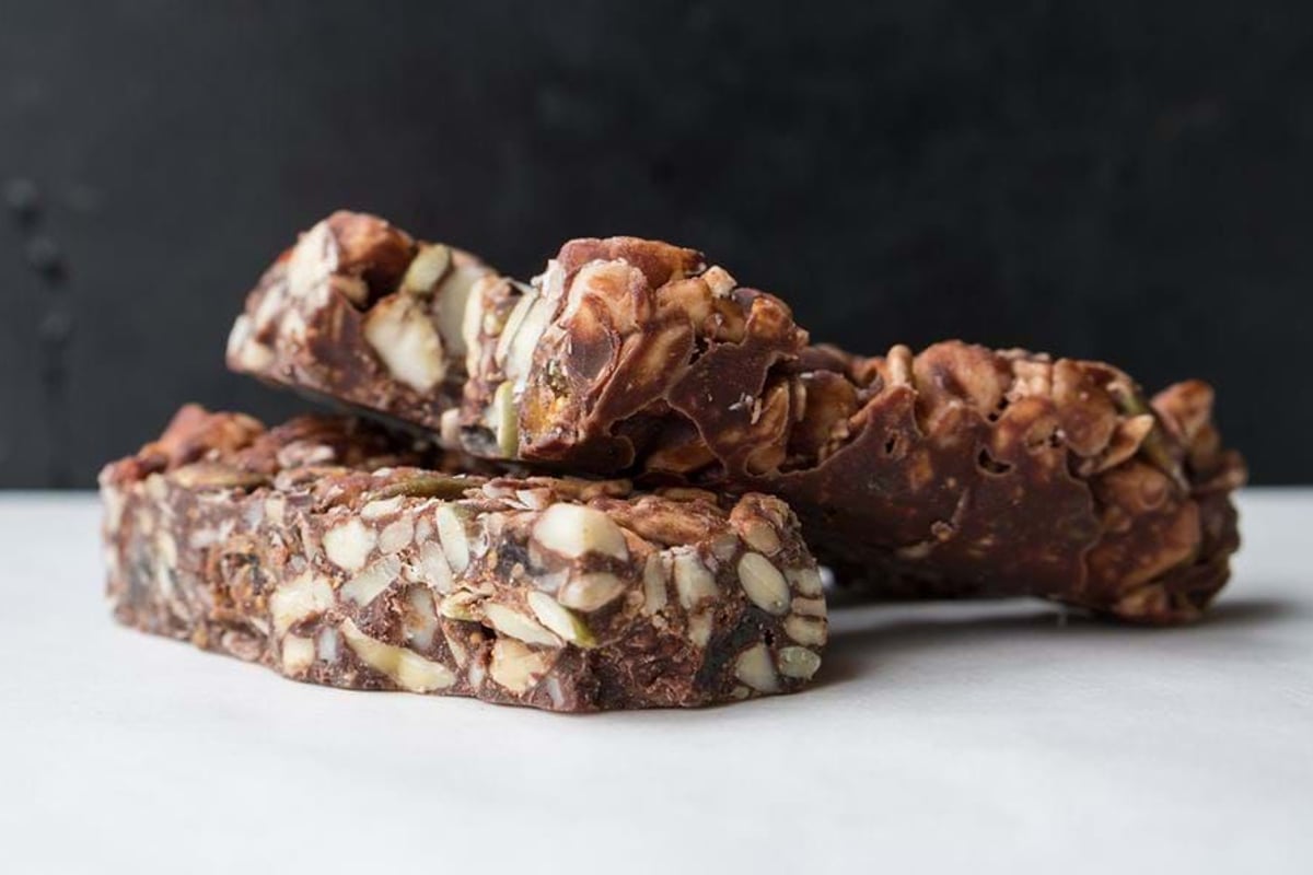 Two stacked nut and chocolate bars on a white surface with a dark background