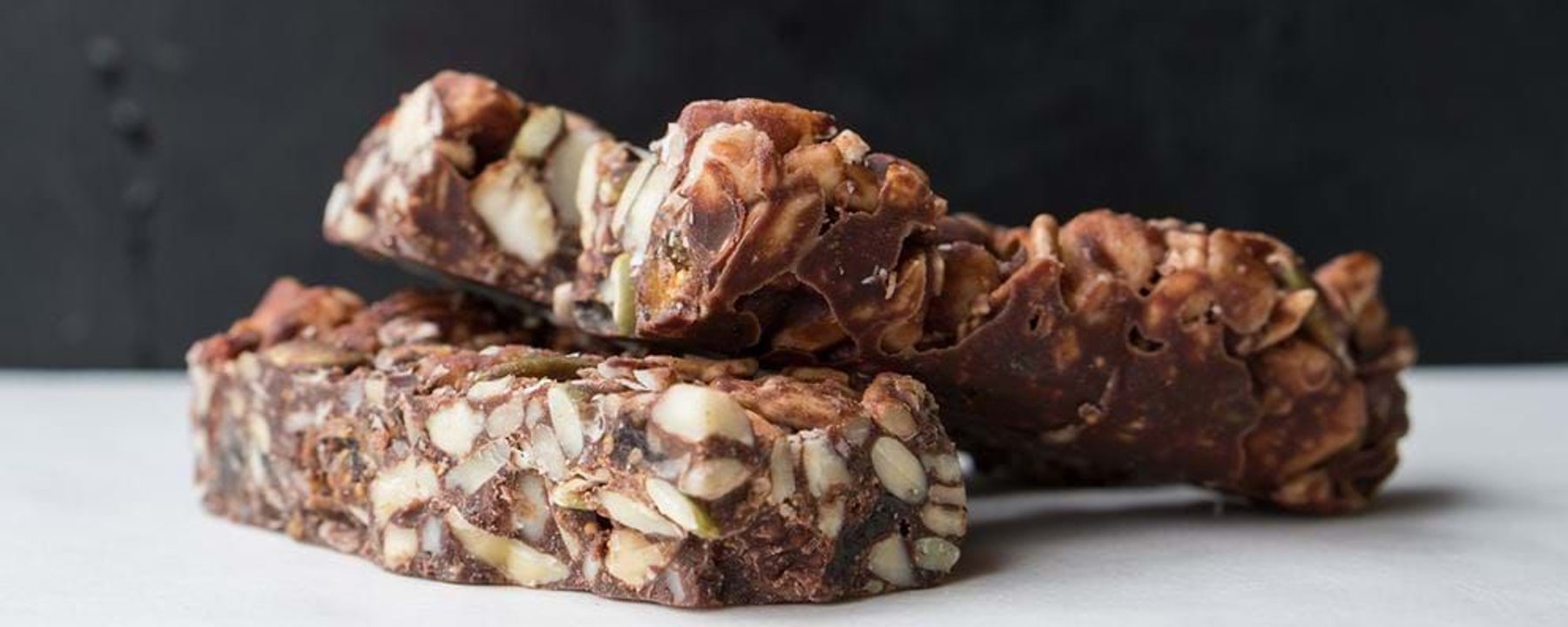 Two stacked nut and chocolate bars on a white surface with a dark background