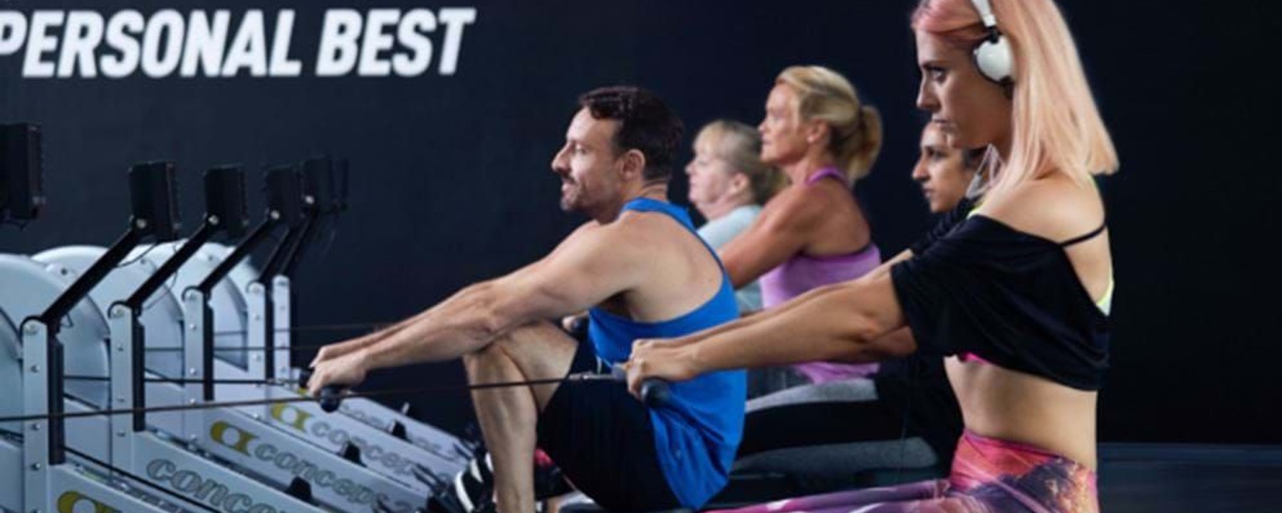 Five people exercising on rowing machines in a gym with motivational text on the wall