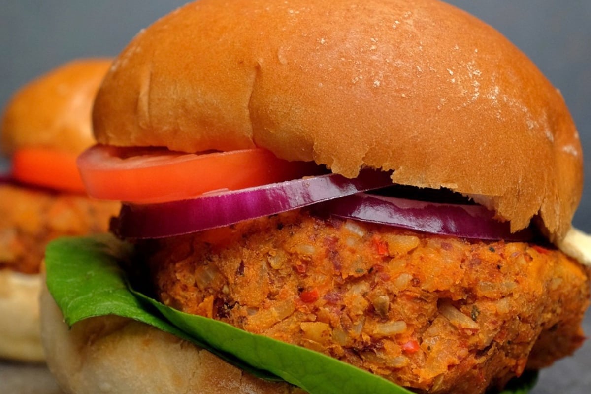 Vegan burger with lettuce, tomato, and red onion in a soft bun on a grey surface