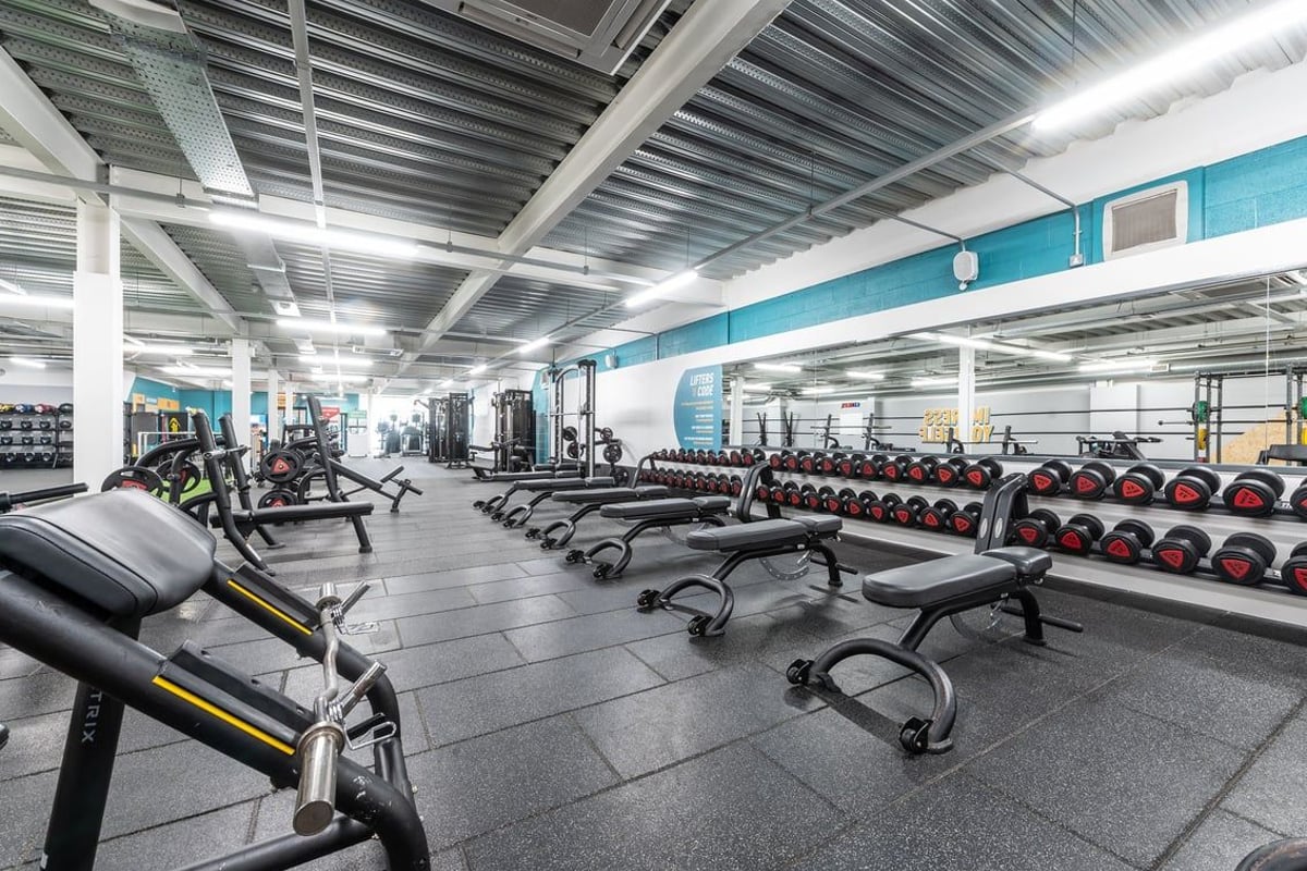 PureGym Banbury Cross Retail Park: Weightlifting area with benches, dumbbells, weight plates, and rubberized flooring.