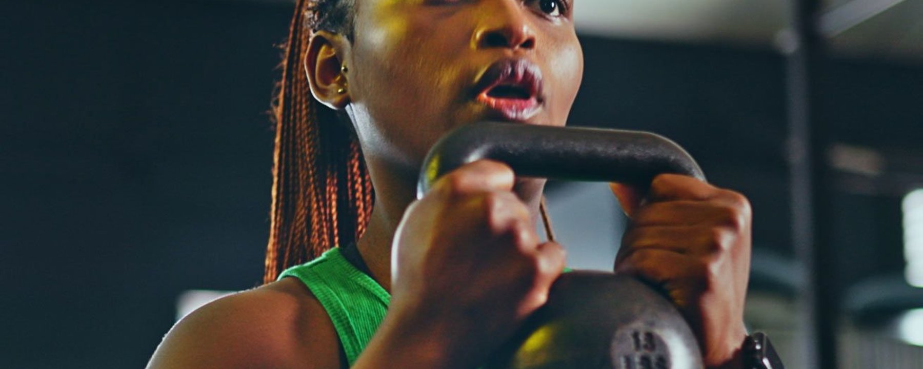 Frau im grünen Top hebt 6 kg Kettlebell im Fitnessstudio