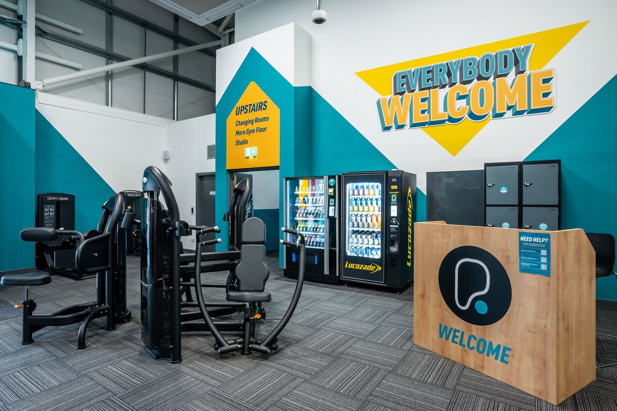 PureGym Market Harborough: Resistance machines, free weights, vending machines, and a welcome sign in a gym studio setting.