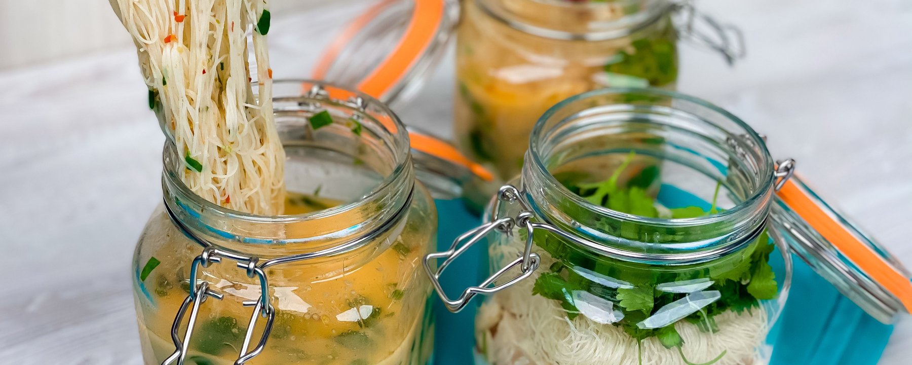 Rice noodles being lifted from glass jar filled with broth and vegetables