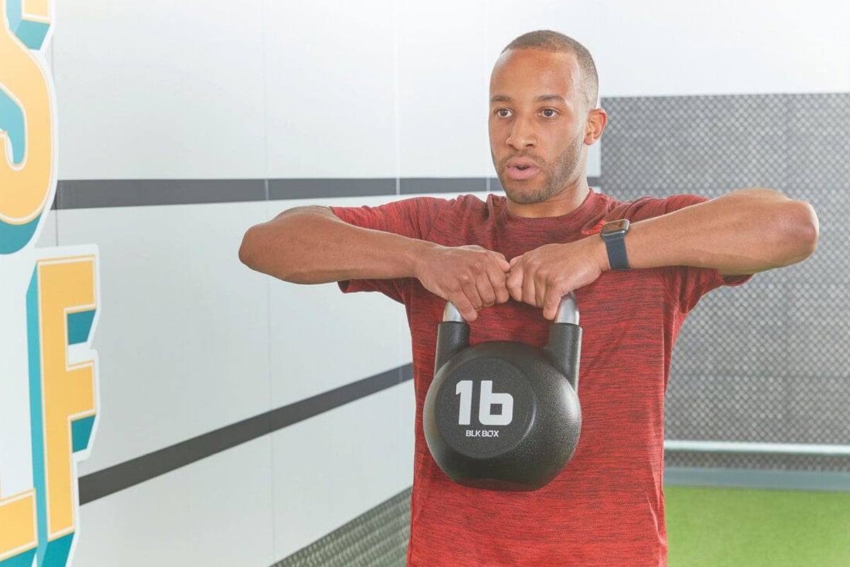 Man in red shirt lifting a 16-pound kettlebell in a gym with motivational wall art