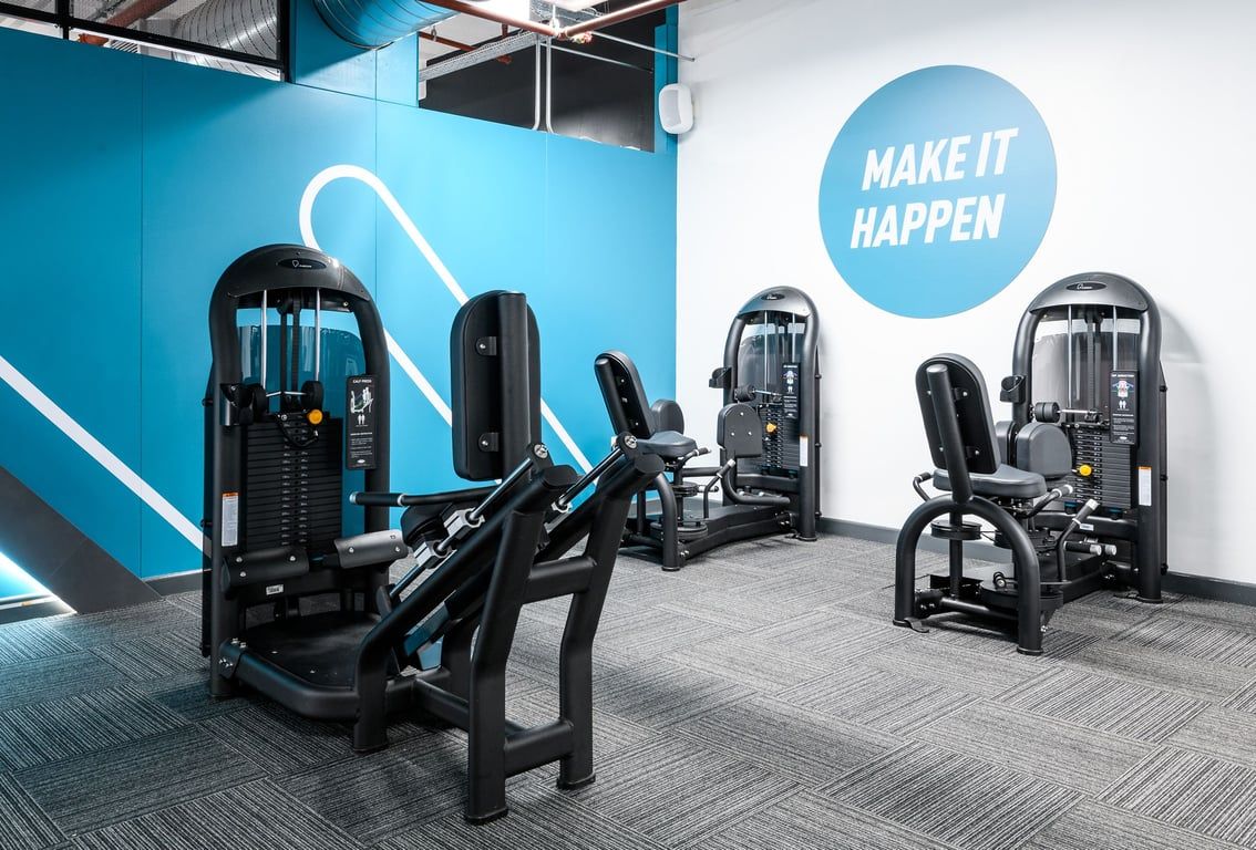 PureGym Cambridge Grafton Centre: Resistance machines in blue color scheme with motivational signage "Make it happen."