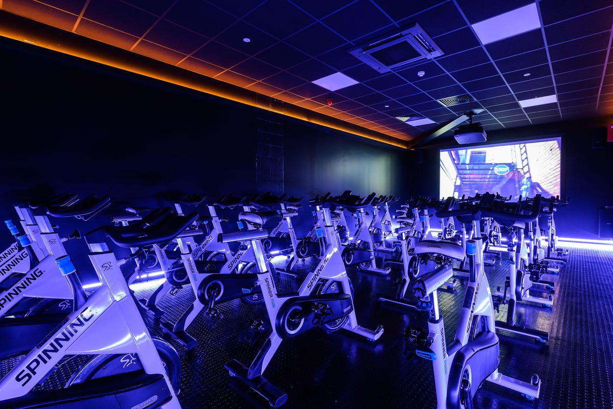 PureGym Salisbury: Rows of stationary bikes inside a dimly lit studio with orange and purple accent lighting.