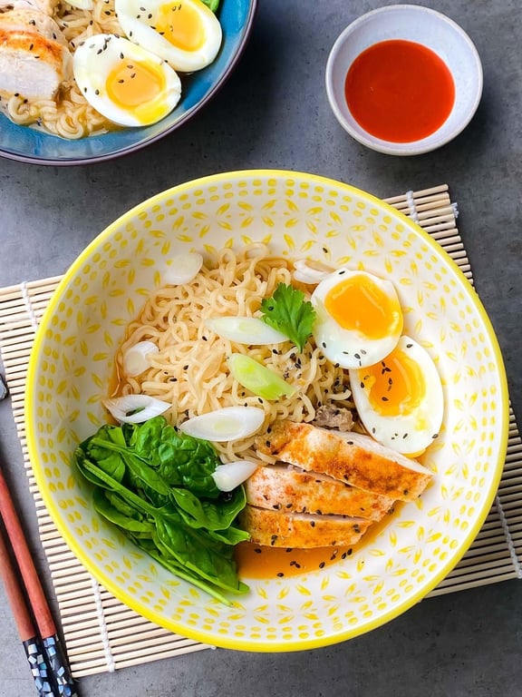 Ramen noodles with boiled eggs, grilled chicken, spinach, spring onions, and sauce bowl