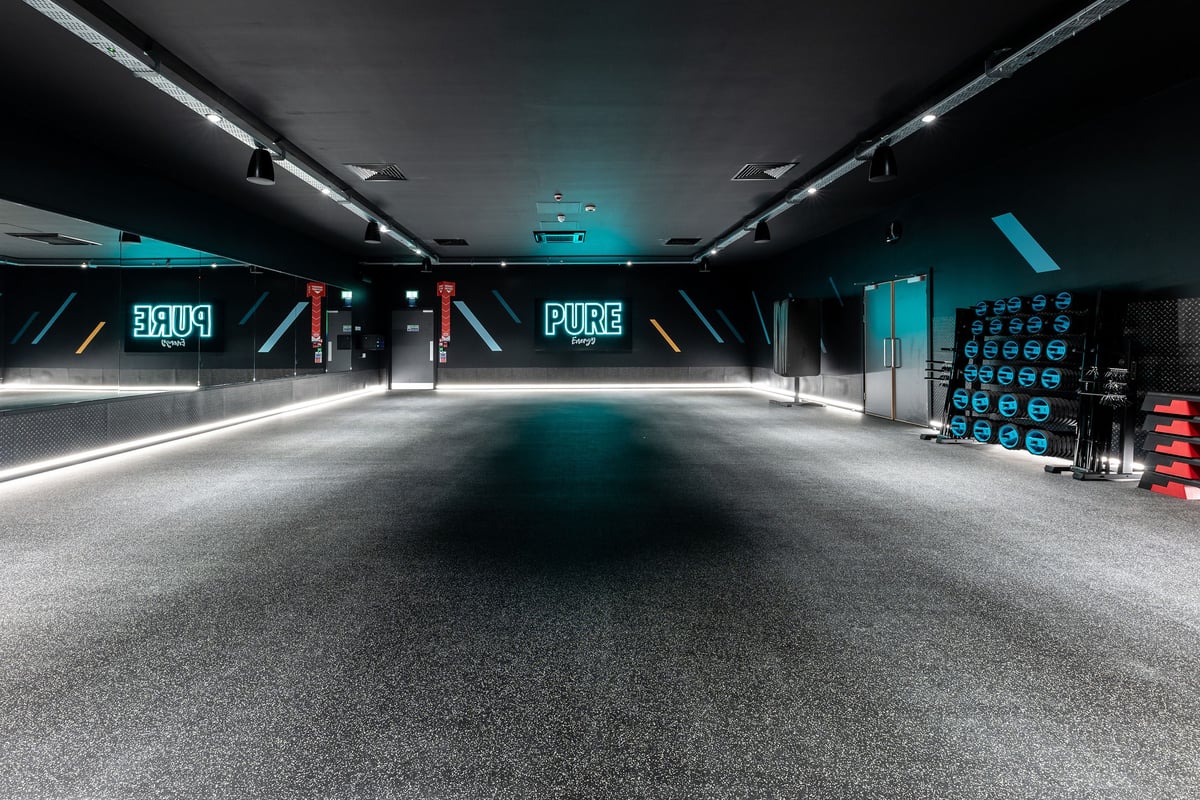 PureGym Maidenhead: Futuristic studio with neon lights, weight racks, and vending machines along walls.