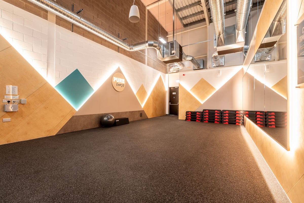 PureGym Shepton Mallet: Rubberized flooring, angled geometric wall designs, cubbies with red bins lining walls.