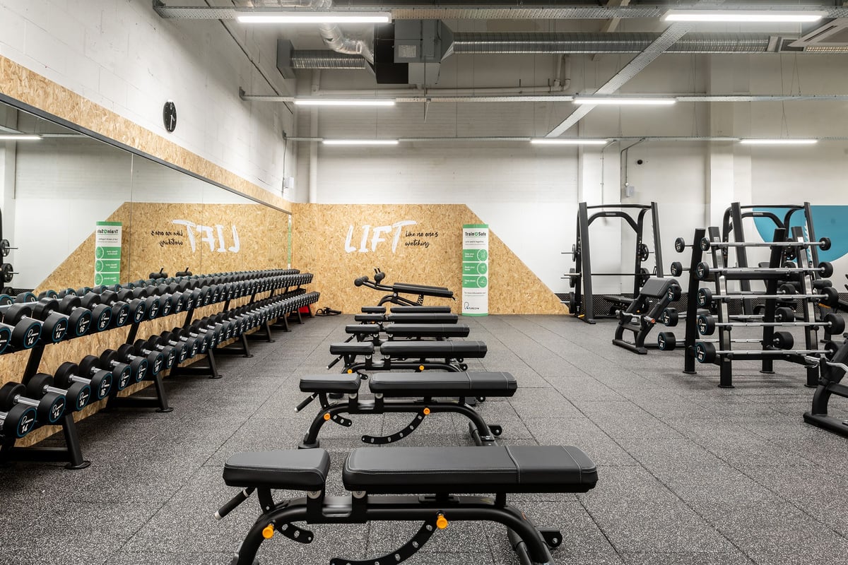 PureGym Ashford Warren Retail Park: Rows of benches, free weights, squat racks, and rubberized flooring in a gym studio.