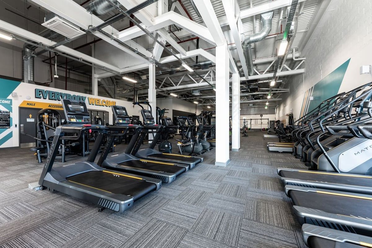 PureGym Rushden: Rows of treadmills, ellipticals, signage for EveryBeat and exposed ceiling structure.