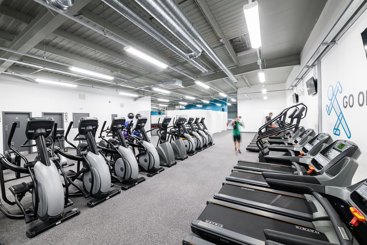 PureGym Aberdeen Wellington Circle: Rows of stationary bikes and treadmills in a bright gym space with exposed ceiling ducts.