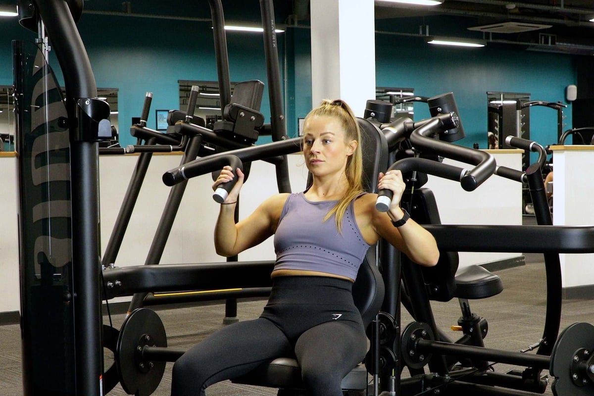 Woman in purple sports top using chest press machine in gym with turquoise walls