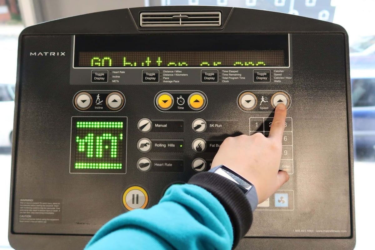 Hand pressing speed increase button on treadmill control panel with digital display