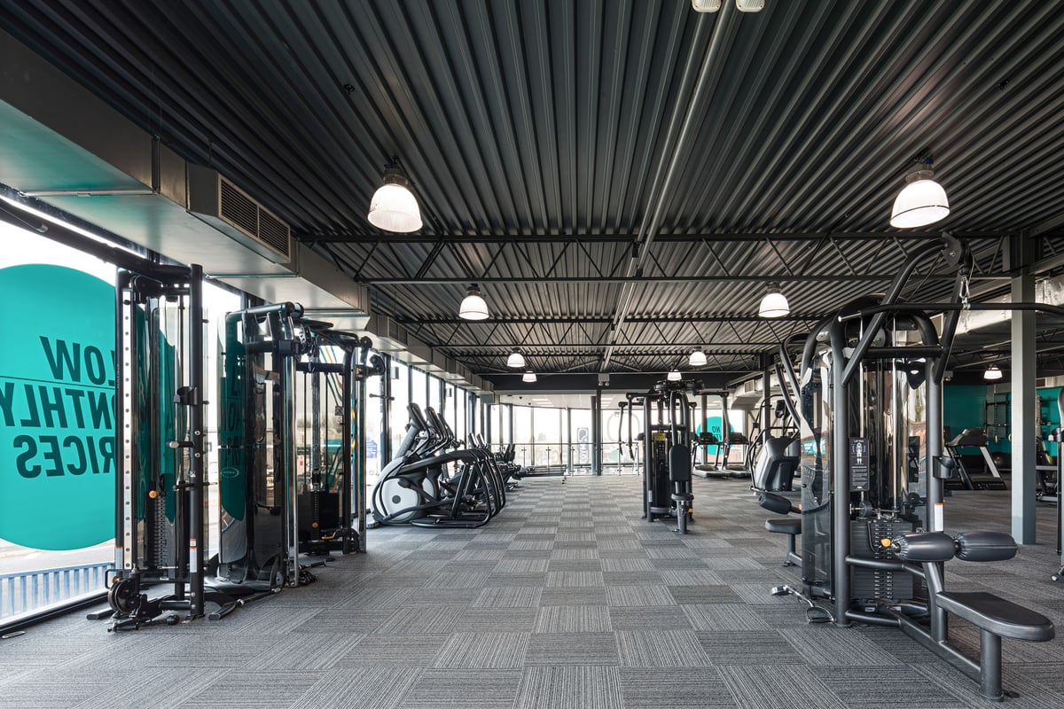 PureGym Dudley Tipton: Gym floor with squat racks, weight machines, rubberized flooring, and industrial ceiling lamps.
