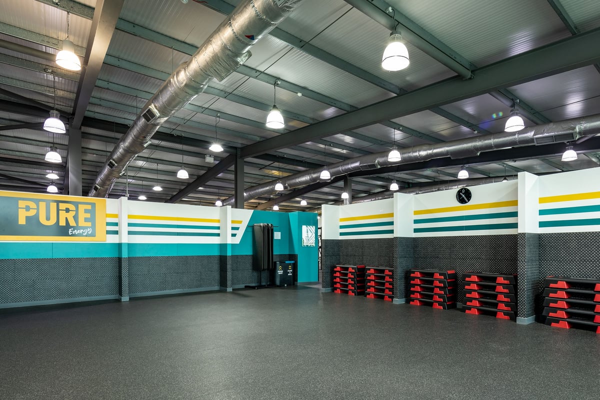PureGym Cardiff Gate: Rubberized flooring, weight plates, benches and mirrors in a teal and yellow studio interior.